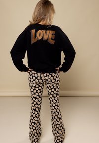 Zwarte sweatshirt met glinsterende gouden "LOVE" tekst op de achterkant, gecombineerd met zwarte uitlopende broek met een beige bloemenpatroon.