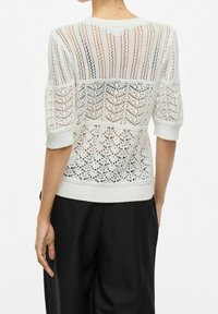 Maglione lavorato a maglia crema con design a traforo, caratterizzato da maniche corte, scollatura e orlo a coste e un motivo testurizzato e sovrapposto.