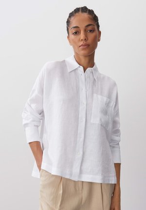 White linen long-sleeve shirt with button front, pointed collar, and single chest pocket. Loose fit and slightly textured fabric.