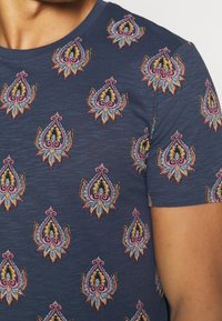 Mörkblå kortärmad t-shirt med färgglada paisleymönster broderade över hela tyget. Tyget har en strukturerad, något melerad yta.