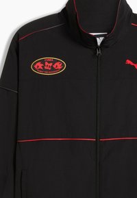 Sort zip-up jakke med røde detaljer og et Sonic the Hedgehog-logo patch på brystet. Har en høj krave og letvægtsstof.