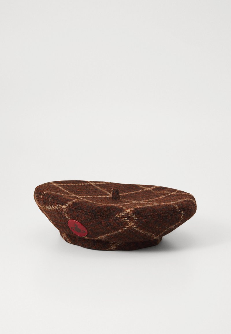 Ruskea villa-baret jossa on tarkistuspinta, joka on varustettu pienellä keskusnapilla ja punaisella logopatchilla sivulla. Pehmeä rakenne, pyöreä tasainen muoto.