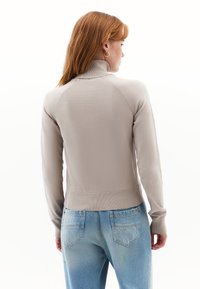 Licht beige pullover met een hoge kraag, ribbelzoom en lange mouwen, gedragen over lichtblauwe jeans. Zachte textuur en aangesloten ontwerp.