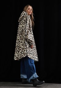 Poncho con capucha de gran tamaño en estampado de leopardo, hecho de una tela suave, con mangas largas y un dobladillo curvado. Combinado con jeans acampanados y botas negras.