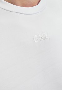 Fehér, rövid ujjú póló sima pamutból, puha, kerek nyakkivágással és fehér, dombornyomott "CNZ" logóval a mellkas területén.