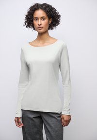 Haut à manches longues en tissu gris clair avec un col rond, associé à un pantalon à carreaux gris avec un motif écossais.