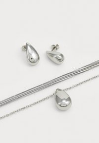 Les boucles d'oreilles pendantes argentées et le collier assorti présentent des designs lisses en forme de goutte d'eau. Le collier est équipé d'une chaîne délicate avec un accent texturé.