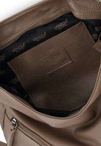 Brown leather handbag interior with a textured finish, featuring a black lining marked "VENEZIA" and a zippered pocket.