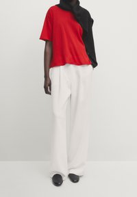 T-shirt rouge à manches courtes sur un pull noir, associé à un pantalon large blanc et des ballerines noires, mettant en valeur un look décontracté et superposé.