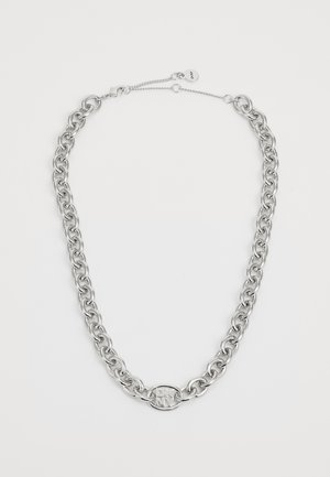 Collier chaîne en argent avec pendentif ovale logo DKNY et fermoir ajustable sur fond blanc.