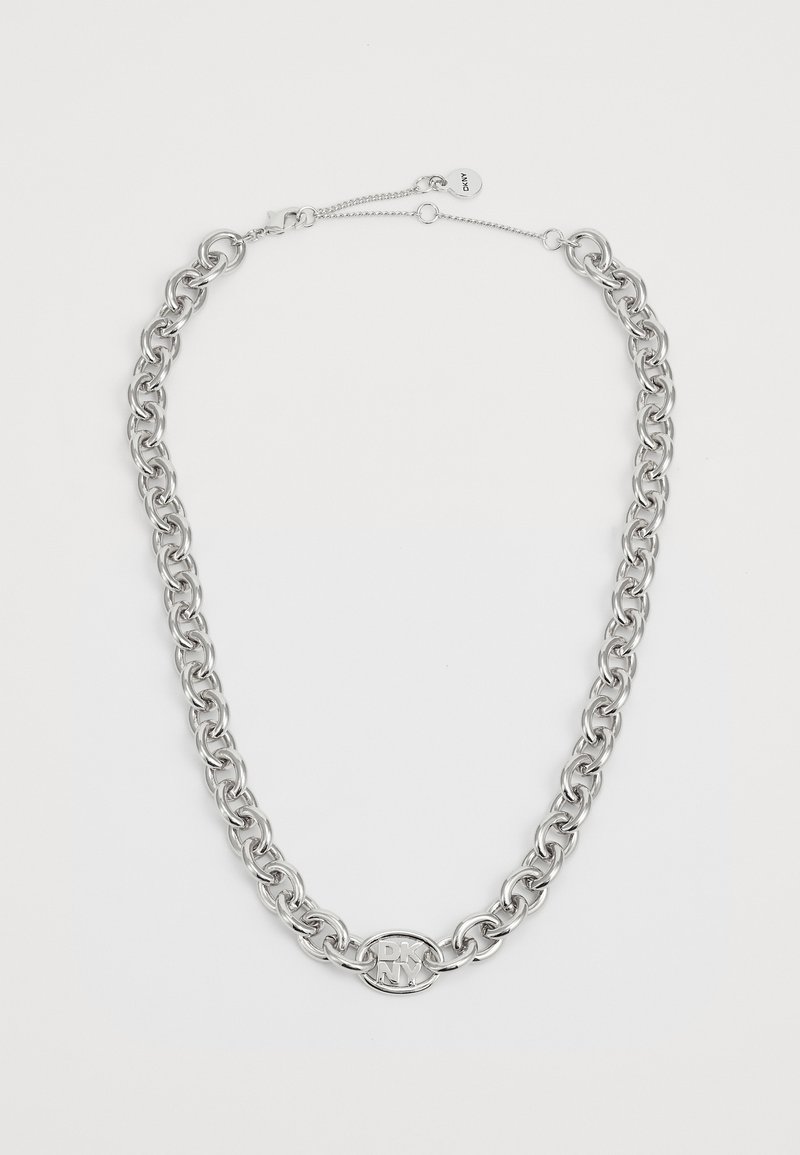 Collier chaîne en argent avec pendentif ovale logo DKNY et fermoir ajustable sur fond blanc.
