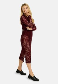 Bordo čipkasta obleka z dolgimi rokavi in stranskimi razporki, ki ima cvetlične vzorce. Nošena s črnimi loaferji, ki poudarjajo njeno polprosojno teksturo.