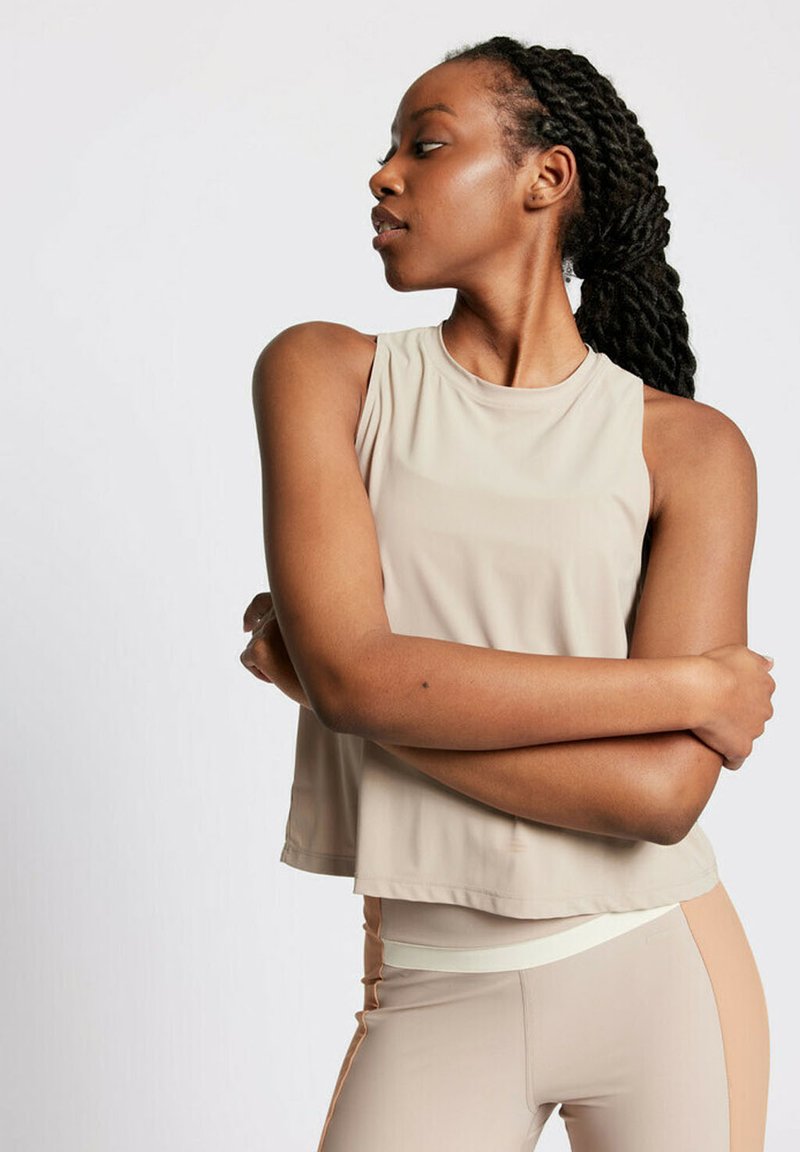 Beige ärmelloses Cropped-Top mit glatter Textur, Rundhalsausschnitt und minimalen Nähdetails, kombiniert mit körpernahen hellen Leggings.