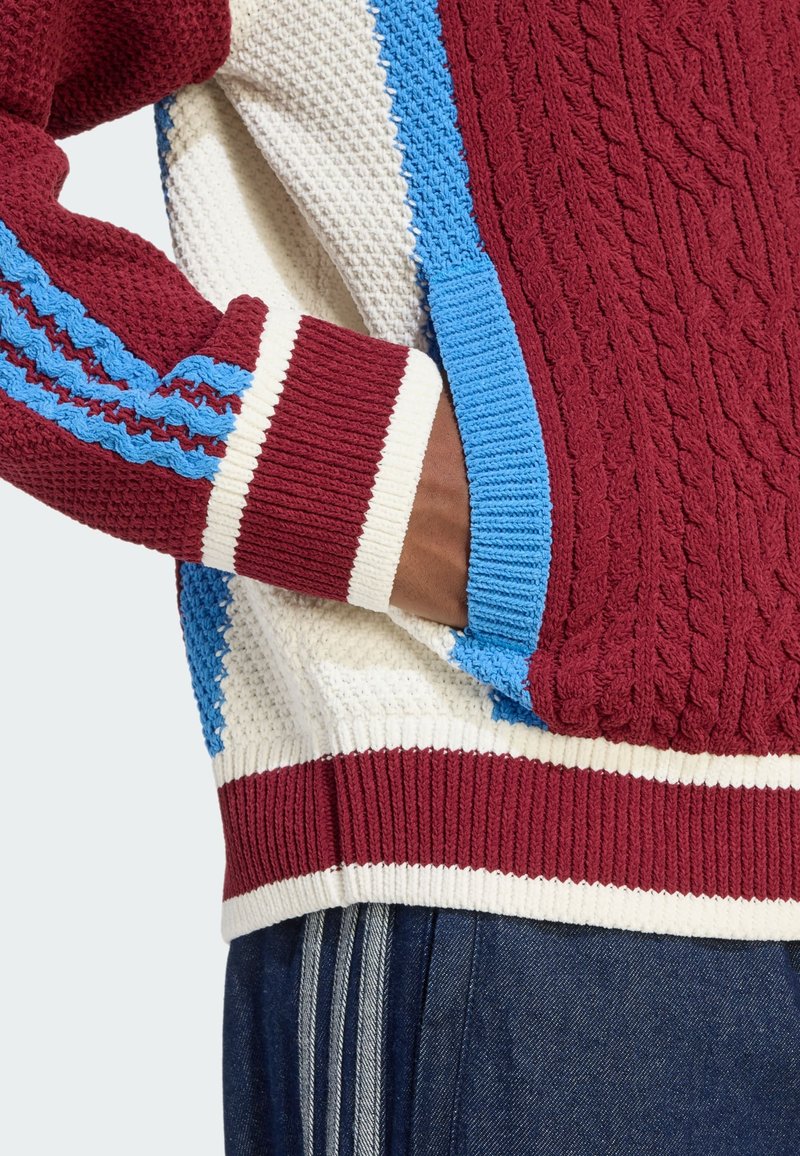 Rood, wit en blauw gebreid vest met een kabelpatroon, geribbelde manchetten en een zak aan de zijkant. Zachte textuur met contrasterende strepen.