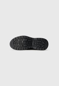 Semelle de chaussure en caoutchouc noir avec un motif de semelle profonde et un texte moulé. Présente diverses textures et motifs pour une meilleure traction et durabilité.