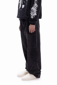 Black oversized denim jeans with a slightly textured finish, paired with a black graphic hoodie and white slip-on shoes.