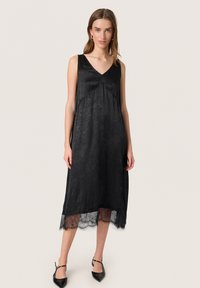 Schwarzes ärmelloses Kleid mit V-Ausschnitt, strukturiertem Stoff und Spitzenumschlag. Die Silhouette ist locker, reicht bis zur Mitte der Waden und hat einen fließenden Schnitt.