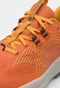 Bright orange athletic shoe with textured upper, yellow laces, and rubber sole. Features patterned accents and reinforced eyelets.