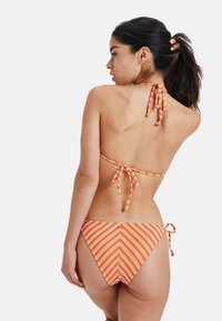 Dwuczęściowy strój kąpielowy w pomarańczowo-białe paski; góra nawiązująca na szyję z wiązaniami, dopasowane, niskie majtki z wiązaniami po bokach i wzorem w jodełkę.