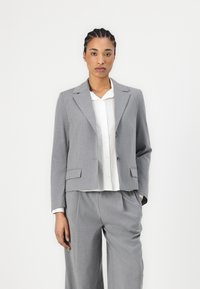 Grå skreddersydd blazer med notched lapels, to knapper og frontlommer, parret med en hvit skjorte med knapper og matchende grå bukser.