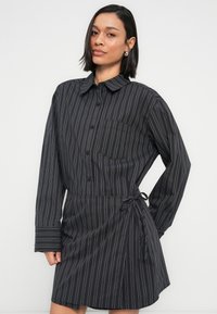 Φόρεμα πουκάμισο με μαύρες ρίγες, γιακά, μακριά μανίκια, τσέπη και ζώνη στη μέση για ρυθμιζόμενη εφαρμογή. Ομαλή υφή υφάσματος.