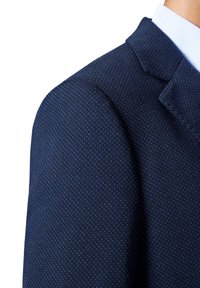 Granatowa marynarka z fakturowanej tkaniny z małymi, subtelnymi wzorami. Widać wyraźne ramiona i detale w postaci klap.