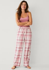 Lichtroze tanktop met kantafwerking, gecombineerd met brede, geruite pyjamabroek in roze en wit, met een elastische tailleband en een trekkoord.