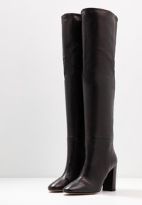 Sorte læderstøvler over knæet med en glat tekstur, spids snude og kraftig hæl. Simpelt design uden synlige beslag eller detaljer.
