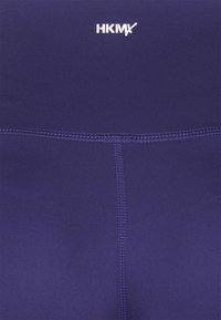 Granatowe legginsy sportowe z gładkiego, elastycznego materiału. Oferują białe logo w talii oraz płaskie szwy wzdłuż szwów.