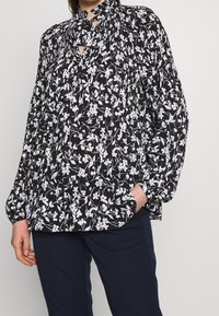 Black and white floral blouse with a high neck and keyhole detail, featuring puff sleeves and a loose fit. Smooth fabric and delicate pattern.