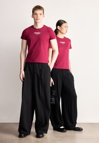 Kaštanově červená bavlněná trička s logem "TOMMY", kombinovaná s černými širokými kalhotami. Model má doplňky v podobě malé černé kabelky a balerínek.