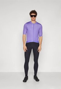 Μωβ κοντομάνικη φανέλα ποδηλασίας με μπροστινό φερμουάρ, συνδυασμένη με μαύρα κολάν ποδηλασίας. Ο υφασμάτινος σχεδιασμός και η εφαρμοστή γραμμή βελτιώνουν την απόδοση.