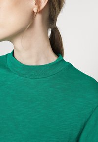 Pullover verde in cotone con un collo alto e una texture morbida. Presenta un colore uniforme senza motivi, mostrando una vestibilità comoda e un design semplice.