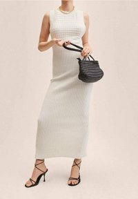 Dzianinowa, bezrękawnikowa, ryflowana maxi sukienka w kolorze off-white z dopasowanym korpusem. Uzupełniona o małą czarną plecioną torebkę oraz czarne sandały na obcasie.