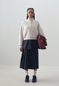 Svetlo siva skrajšana trenerka z visokim ovratnikom, v kombinaciji s črno kratkimi krili. Črne superge z modrimi detajli in belimi nogavicami. Burgundska torba.