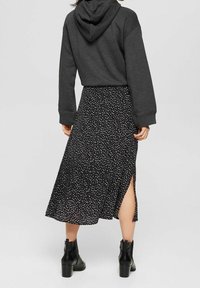 Černá dlouhá sukně s bílými puntíky a rozparkem na boku; doplněná tmavě šedou krátkou mikinou s kapucí. Celý outfit doplňují černé kotníkové boty.