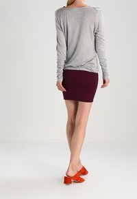 Maglietta grigia a maniche lunghe con vestibilità rilassata, abbinata a una gonna aderente bordeaux. Le scarpe sono in suede arancione con tacco a blocco.