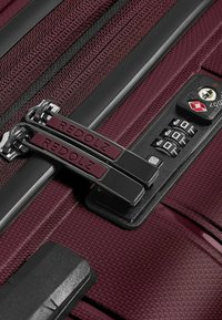 Valigia bordeaux in primo piano con tessuto texturizzato, doppi zip argentati etichettati "REDOLZ", una serratura a combinazione e dettagli in hardware scuro.