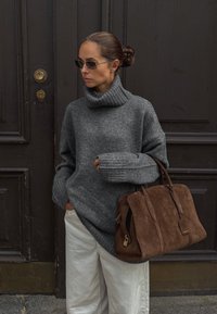 Jersey de cuello alto de punto gris con puños acanalados; corte holgado; combinado con pantalones color crema. Lleva un bolso de ante marrón con acentos de cuero.