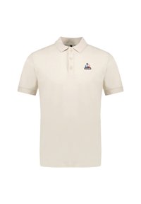 Polo beige hecho de algodón, con un cuello clásico, tres botones y un pequeño logo bordado en el lado izquierdo del pecho.