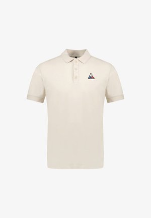 Polo beige hecho de algodón, con un cuello clásico, tres botones y un pequeño logo bordado en el lado izquierdo del pecho.