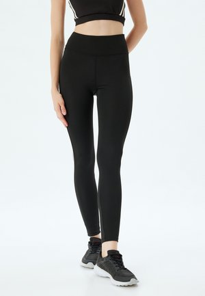 Zwarte hoge tailleleggings gemaakt van rekbaar materiaal, met een aansluitend ontwerp en naadloze constructie. Gekoeld met zwarte sportschoenen.