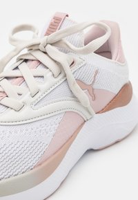 Sneaker Puma bianca e rosa pallido con tomaia in maglia, robusta suola bianca, lacci annodati e logo Puma ben visibile sul lato.