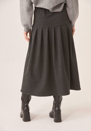 Mujer vistiendo una falda midi gris con estampado, suéter gris y botas de cuero negras con tacón, fotografiada desde atrás.