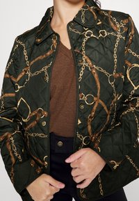 Zelená prošívaná bunda se vzorem zlatého řetězu a kožených popruhů. Obsahuje patentky a klasický límec. Hnědá pletená podšívka je viditelná.