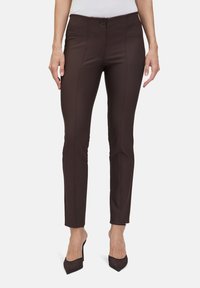 Brązowe dopasowane spodnie wykonane z teksturowanej tkaniny, z zamkiem na guziki z przodu i widocznymi szwami. Połączone z czarnymi szpilkami.