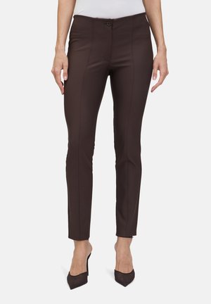 Bruine slim-fit broek van een textuurstof, met een sluiting met een voorknop en zichtbare stiknaaddetails. Gecombineerd met zwarte hakken.
