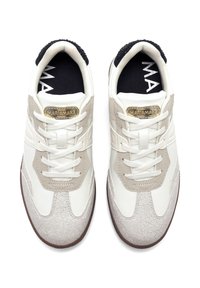 Sneaker aus weißem Leder mit beigen Wildlederakzenten und einem strukturierten, rissigen Muster. Verfügt über eine abgerundete Zehenpartie und flache Schnürsenkel. Goldenes Logosymbol auf der Zunge.