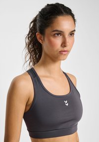 Donkergrijze sportbeha met een gladde textuur, brede banden en een slimfit ontwerp. Bevat een klein wit logo aan de voorkant.