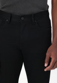 Črne denim hlače z oprijetim krojem, petimi žepi, z gumbom za zapiranje in subtilnimi šivi. Gladka tekstura, brez vidnih vzorcev.
